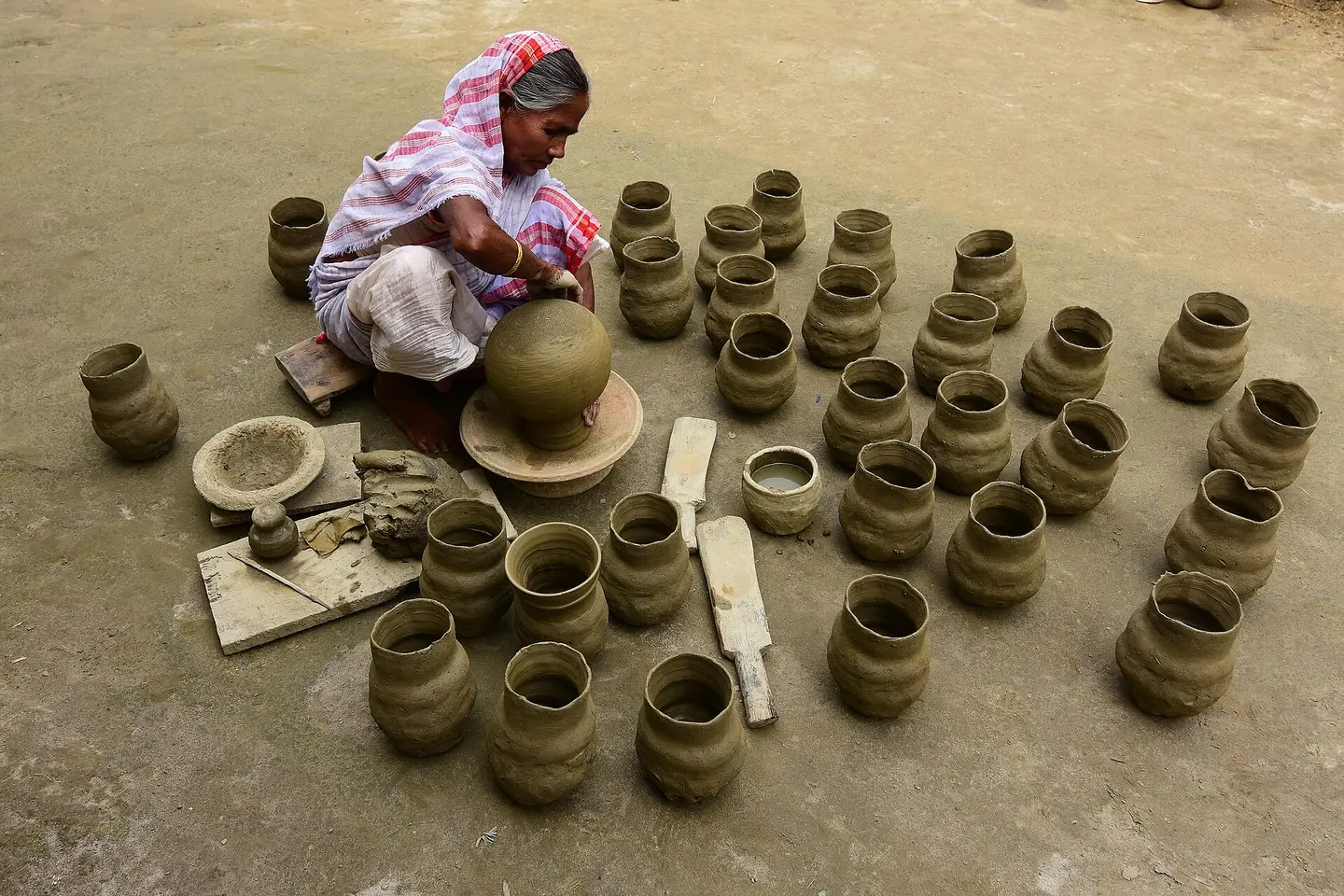 A potter shaping clay by hand, surrounded by rows of freshly thrown pots drying on the ground